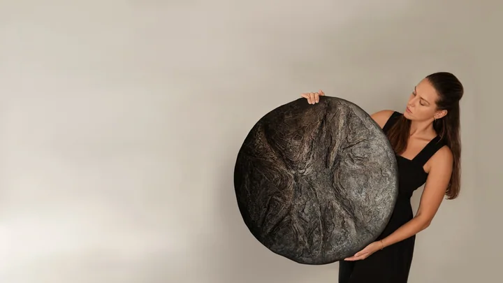 Kseniia holding a dark handmade cement round in her studio